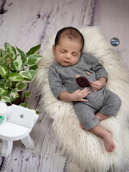 A humorous and modern newborn setup, showing a baby sleeping next to miniature "work from home" props like a laptop and a coffee cup.