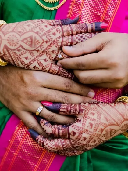 A close-up focusing on the bride's hands, decorated with mehendi and green bangles, wrapped around her fiancé. A beautiful, symbolic shot.