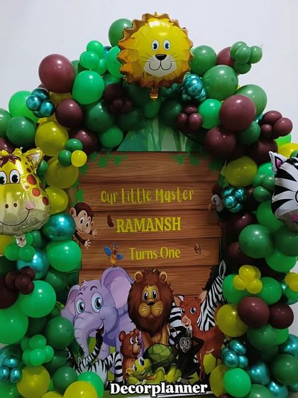 A closer look at the personalized jungle theme backdrop for Ramansh's first birthday. The vibrant greens and cute cartoon animals make it a cheerful and inviting centerpiece for the party.