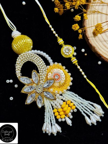 A bright and cheerful yellow floral Rakhi set. The Lumba for the bhabhi is elaborate with a large flower and pearl tassels, perfectly complemented by the simpler rakhi for the brother.