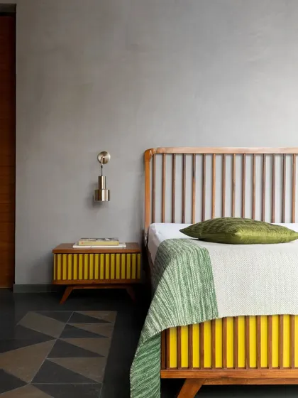 This custom bed and side table continue the theme of clean lines and vibrant color. The vertical slats of the headboard and the pop of yellow create a cheerful, modern look against the calm, grey-plastered walls.