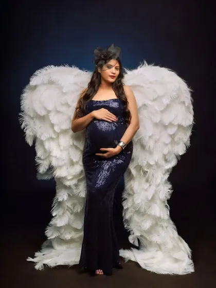 A truly angelic portrait featuring a mom-to-be in a sparkling blue gown, adorned with a magnificent pair of white feathered wings.