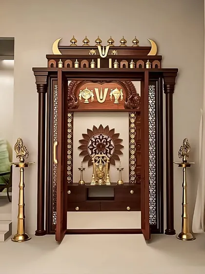 This traditional pooja mandir design features ornate wooden doors with jali work, allowing for privacy while maintaining a sense of openness. The structure is crowned with Vaishnavite symbols and flanked by classic brass lamps, blending functionality with deep-rooted spiritual artistry.