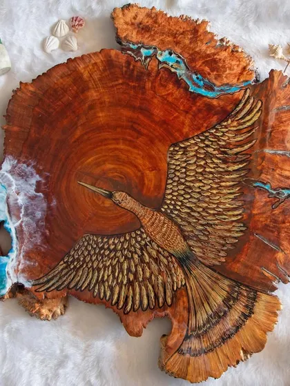 A unique piece combining wood burning art with resin. This large wood slice features a hand-sketched bird with detailed feathers, set against a backdrop of blue resin ocean waves.