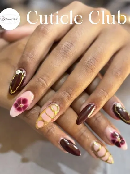 A beautiful and intricate set combining solid maroon nails with hand-painted floral designs and gold accents.