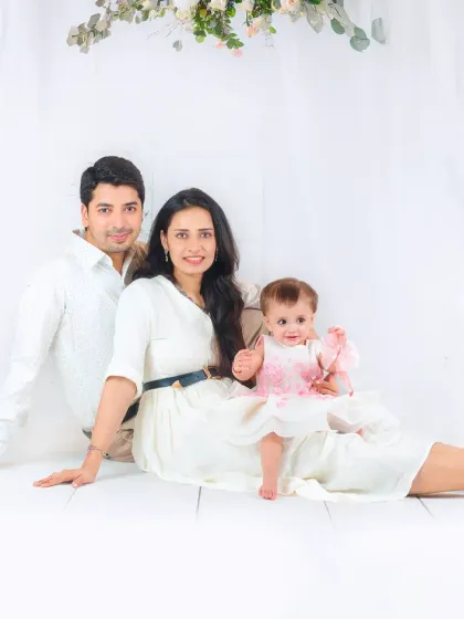 A serene family portrait with parents and their baby girl, all dressed in white. The soft lighting and relaxed poses create a feeling of peace and togetherness.