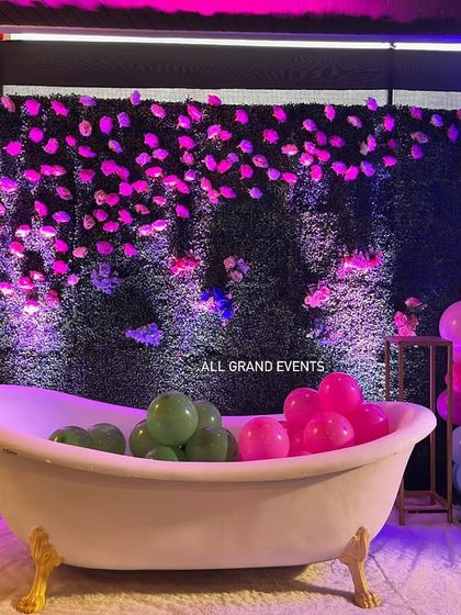 A unique and fun photo prop for a baby shower or birthday. This vintage-style bathtub is filled with colorful balloons and set against a green hedge wall with flowers.