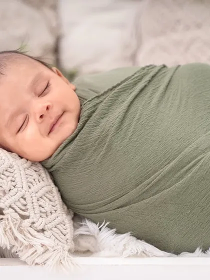 A close-up portrait showcasing a sweet, sleepy smile. The focus is entirely on the baby's peaceful expression.
