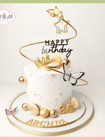 Golden glam for a 35th birthday queen. This white and gold cake is adorned with a spiral topper, butterflies, macarons, and Ferrero Rocher chocolates for a truly luxurious feel.