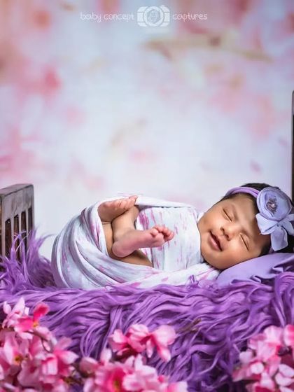 A newborn girl sleeping in a miniature bed surrounded by pink flowers. The soft, dreamy background adds to the fairytale feel of this setup.