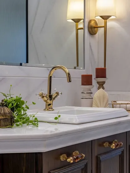A close-up of the vanity in the Thane bathroom, showcasing the detailed hardware, classic gold faucet, and warm lighting. Every detail is meticulously chosen to create a sense of timeless elegance.
