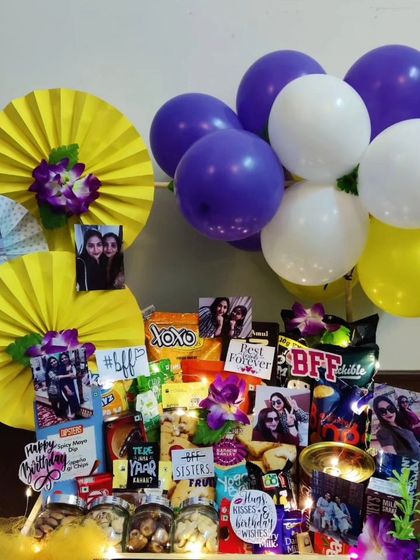 A brightly lit view of the best friend birthday hamper, highlighting the custom photo arrangements and 'BFF' cutouts among the snacks and colorful purple, white, and yellow balloons.