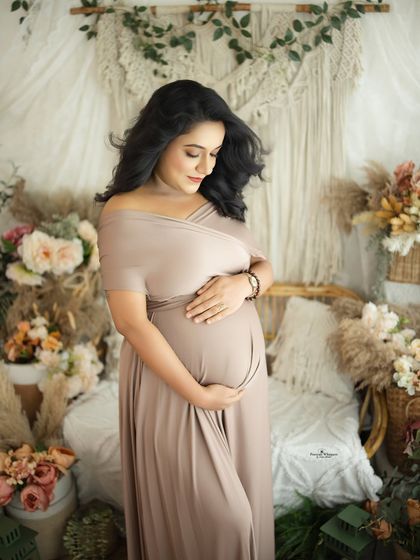 A beautiful solo portrait of a mother-to-be cradling her bump. The soft, earthy tones of the gown and backdrop create a warm and nurturing feel.