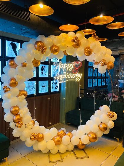 An elegant circular balloon arch in white and gold with a "Happy Anniversary" neon sign, perfect for a stylish anniversary party.