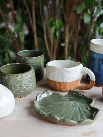 A serene collection of student pieces in shades of green and white, including a leaf shaped plate, textured cups, and a small bud vase.