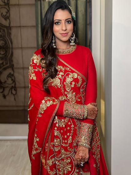 A client looking radiant in a classic red Sabyasachi outfit, her makeup is soft glam with kohl-rimmed eyes.