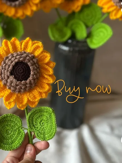 A single crochet sunflower stem with its bright yellow petals and green leaves. The text overlay "Buy now" highlights that these popular items are ready for you to order.