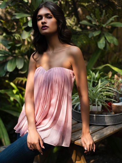 A seated portrait showcasing the soft pink top from It Girl, perfect for a warm summer afternoon.