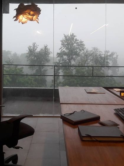 The view from our own studio desk during the Delhi monsoons. The full-height glass wall dissolves the barrier to the outside, making the weather an integral part of the workspace atmosphere.
