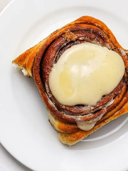 A top-down view of a cinnamon roll with a swirl of frosting. This clean, graphic shot is perfect for menus and social media posts.