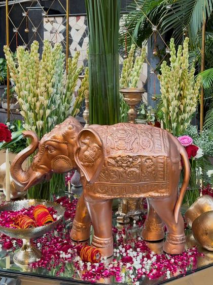 A traditional and ornate detail from a Mata Ki Chowki event. A beautiful copper elephant statue is part of a tablescape decorated with rose petals, marigold strings, and fresh tuberoses.