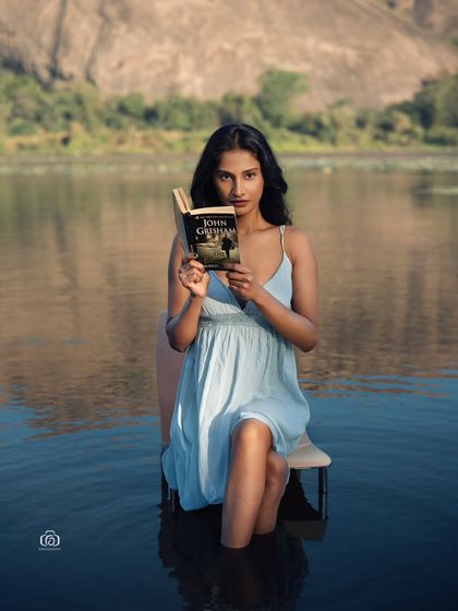A creative and surreal concept, with the model sitting on a chair in the middle of a lake, reading a book. This shot combines fashion with a touch of magical realism.