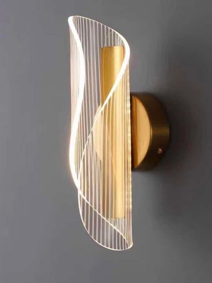 A modern wall sconce with a curved, fluted acrylic shade. The design creates a beautiful play of light and shadow.