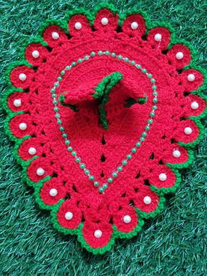 A simple yet beautiful red woolen poshak with a green border and white pearl details. This design is shaped like a leaf or paan, offering a unique look for Bal Gopal.