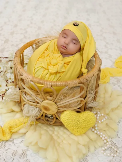 A newborn wrapped in a sunny yellow swaddle, sleeping soundly in a wicker basket. A simple and beautiful setup.