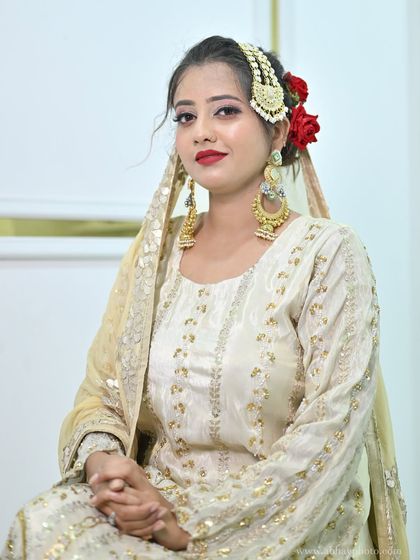 A seated portrait of the model, giving a clear view of the makeup, hairstyle with red roses, and the intricate bridal jhoomar and earrings.