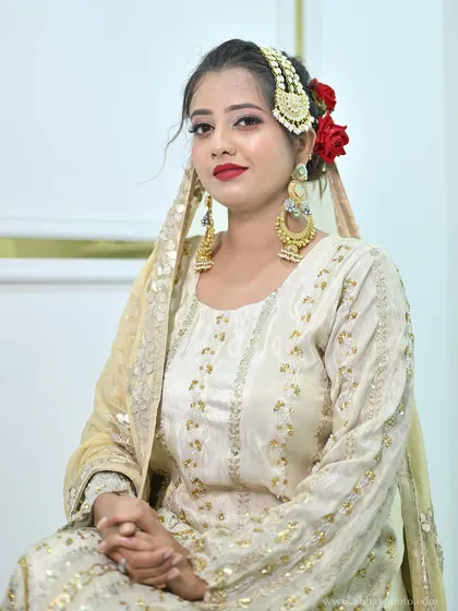 A seated portrait of a model in the ivory sharara set, her hair adorned with red roses and a traditional passa.