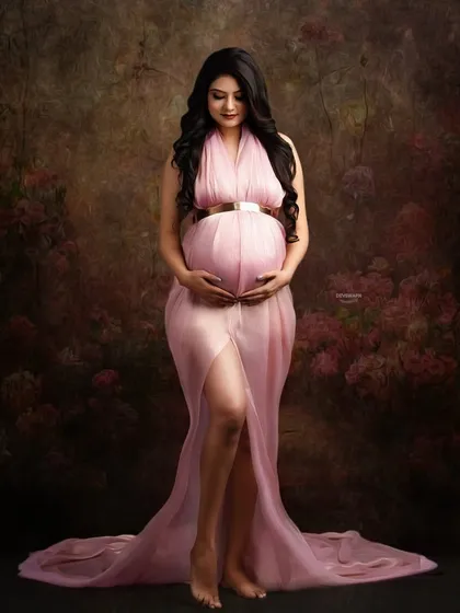 A classic fine art portrait against a painterly brown backdrop. The sheer pink gown, gold belt, and gentle pose evoke a sense of timeless grace and beauty.