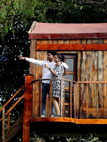 A classic romantic pose on the treehouse set, with the couple looking out towards their future together. The natural surroundings add to the charm of the photo.