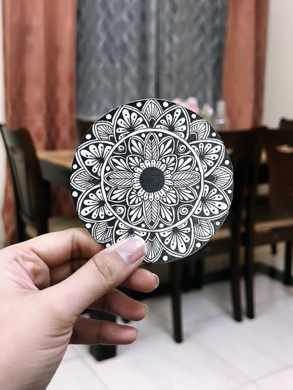 Here is a classic black ink mandala on a circular coaster-sized paper. The high contrast of the black and white design makes every detail of the pattern stand out.