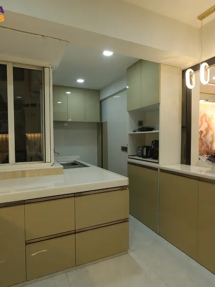 This luxurious kitchen in Thane features beige glossy cabinets, a white countertop, and an open layout that connects to the living area.