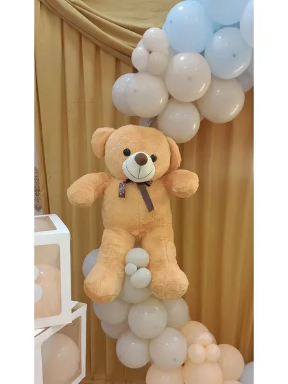 A soft teddy bear prop nestled into the balloon garland on the welcome ring.