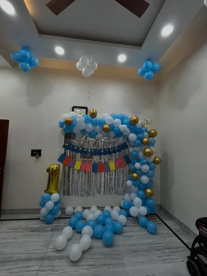 A simple and sweet first birthday decoration for a home party. This setup includes a blue and white balloon arch, a silver foil curtain, and a '1' foil number.