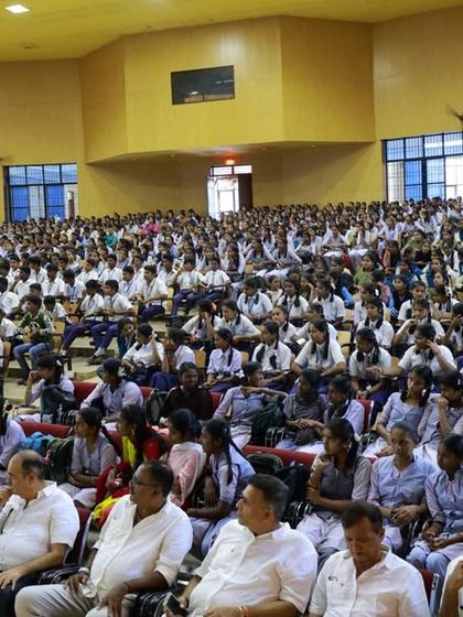 A wide shot of the auditorium packed with students for the MY SEVA TRUST notebook distribution event in Shikaripura. The scale of this initiative shows our commitment.