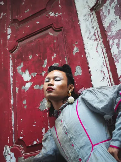 A close-up portrait from the "RIOT" series. The peeling paint of the door complements the model's expressive makeup and defiant gaze, creating a rich, textured image.