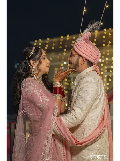 A tender moment captured under the soft glow of string lights. The bride, in her beautiful pink lehenga, shares a loving glance with her partner, creating a classic and elegant nighttime portrait.