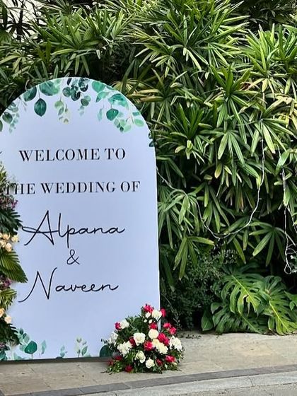 This modern, minimalist welcome sign for a wedding is shaped like an arch and features simple, elegant typography. We added small floral arrangements to the side for a touch of color against the lush green background.