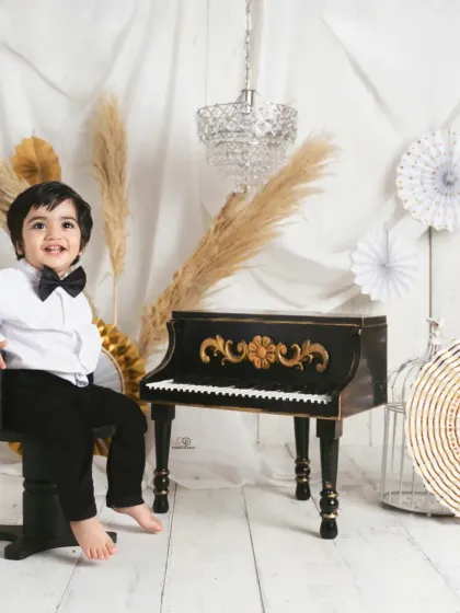 A dapper little gentleman dressed in a bow tie for his 'Pianist' themed session. He poses with a miniature piano, creating a classic and charming toddler portrait.
