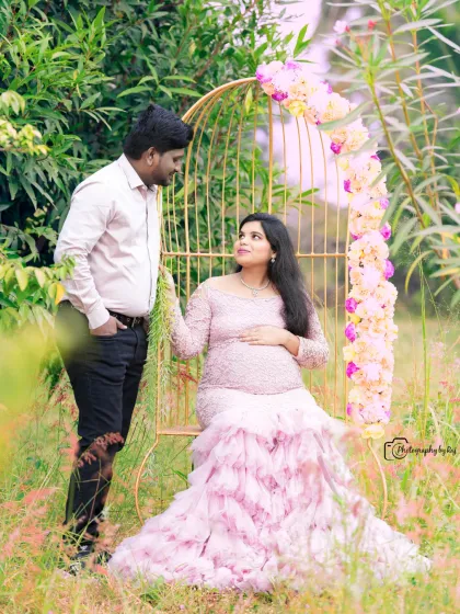 A romantic couple's portrait on a golden birdcage chair. The mother-to-be's pink lace gown and the floral decorations create a fairytale scene.