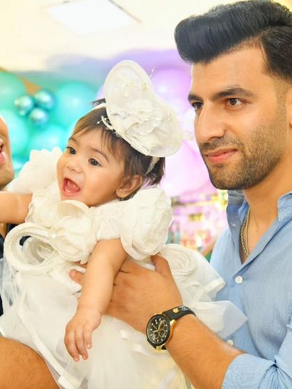 All smiles at the party. This photo captures a sweet moment with the birthday girl being held by family members, with the colorful party decor in the background.