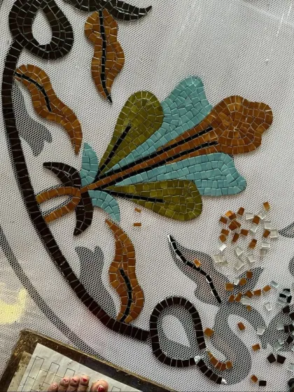 A close-up of the mosaic fresco during its creation, showing the meticulous process of arranging individual glass tiles on a mesh backing before installation.