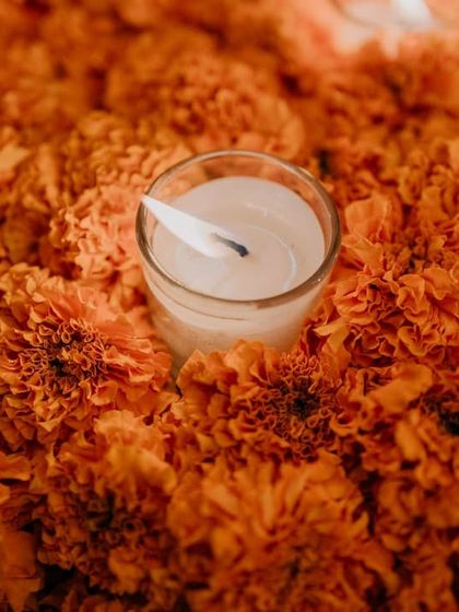 A close-up of a single tea light candle nestled in a bed of bright orange marigolds, a classic and beautiful element of Indian festive decor.