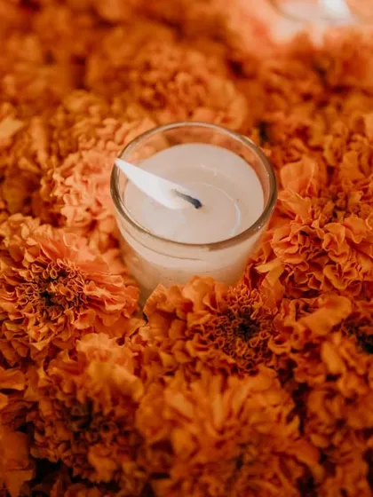 A close-up of a single tea light candle nestled in a bed of bright orange marigolds, a classic and beautiful element of Indian festive decor.