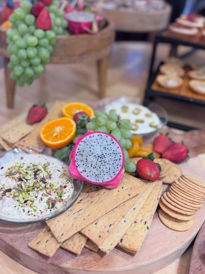 A vibrant platter featuring creamy pistachio dip, multi-grain crackers, and an exotic fruit selection including dragon fruit, strawberries, and grapes. A feast for the eyes and the palate.