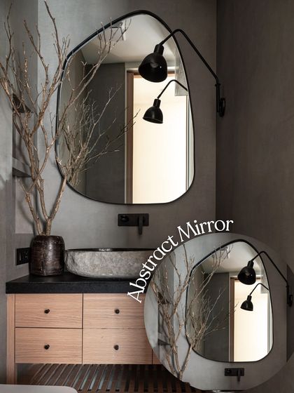 An abstract, organic-shaped mirror serves as a sculptural element in this powder room. Paired with a stone vessel sink and an adjustable wall lamp, it creates a moody and sophisticated atmosphere.