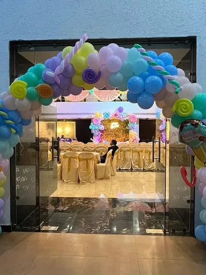 A large, candy-themed balloon archway welcomes guests to the party. This pastel-colored arch is decorated with swirl and donut-shaped foil balloons, setting a sweet tone for the event.